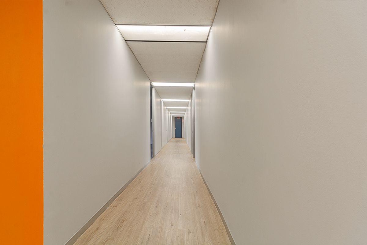 A clean, well-lit commercial hallway featuring wood-look vinyl flooring, suspended acoustic ceiling tiles, and recessed lighting.