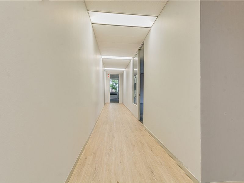 A clean, well-lit commercial hallway featuring wood-look vinyl flooring and recessed ceiling lighting, providing access to adjacent office spaces.