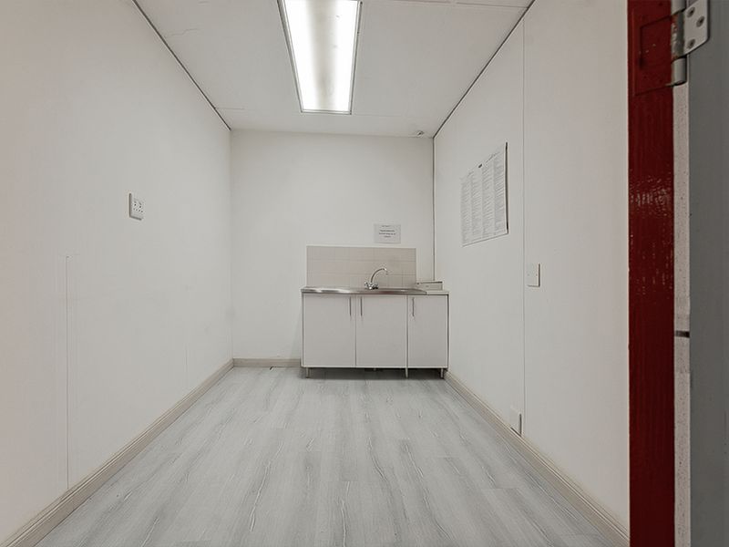 A functional utility space featuring a small sink with base cabinetry, neutral wall finishes, and durable laminate flooring.