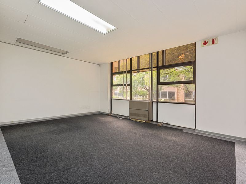 A vacant commercial office space featuring large windows, carpeted flooring, and integrated HVAC unit, suitable for a professional workspace setup.