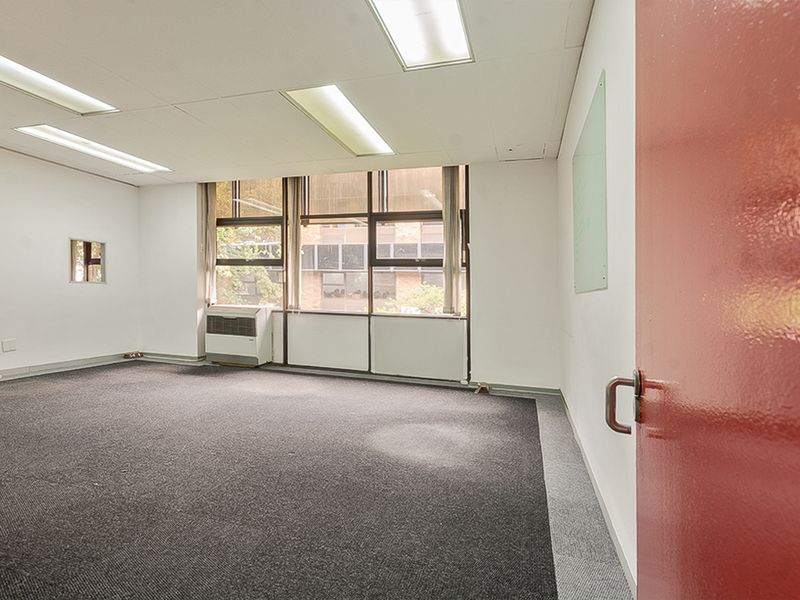 A vacant commercial office space featuring recessed lighting, large windows for natural light, wall-mounted air conditioning, and a glass whiteboard.