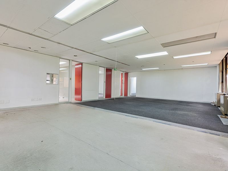 An empty commercial office space featuring a suspended ceiling, recessed lighting, and a combination of carpet and vinyl flooring with internal glass partitions.
