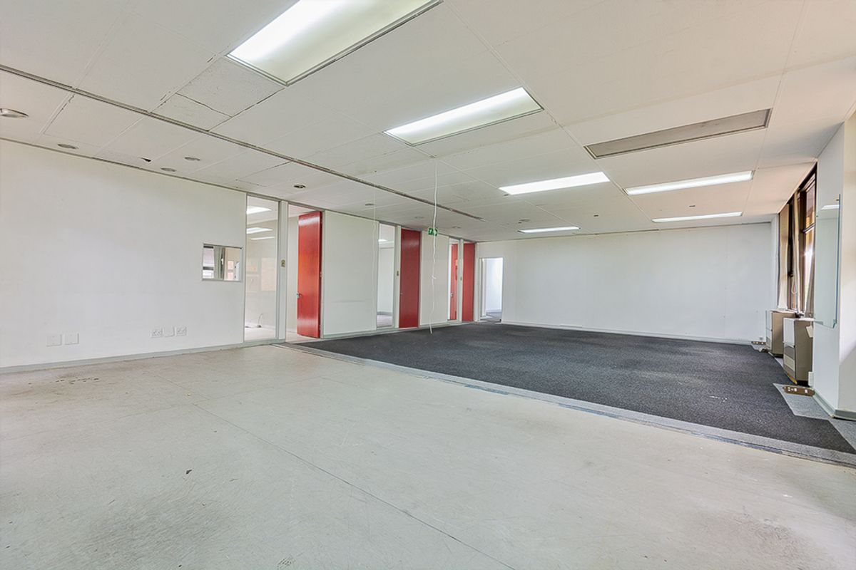 An empty commercial office space featuring a suspended ceiling, recessed lighting, and a combination of carpet and vinyl flooring with internal glass partitions.