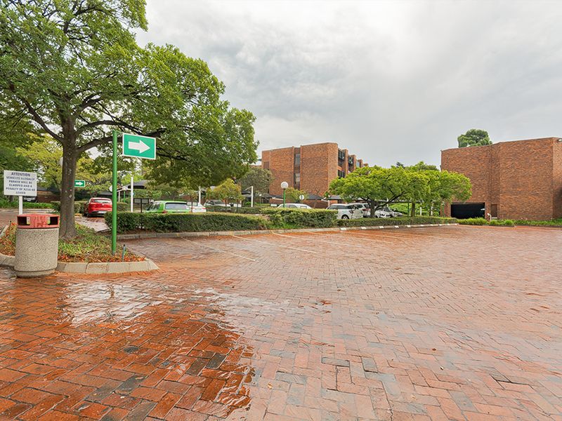 A view of the commercial property exterior featuring a brick-paved parking area, landscaped trees, and multi-story brick building facades.