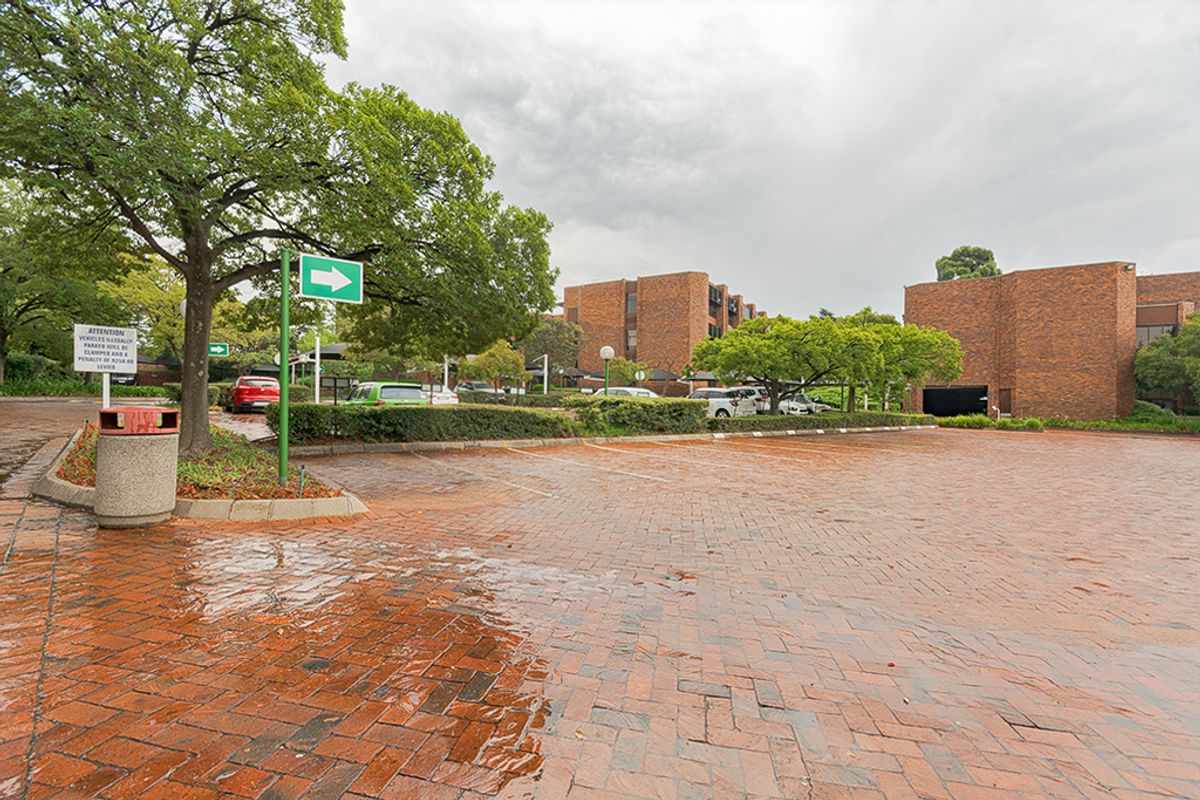 A view of the commercial property exterior featuring a brick-paved parking area, landscaped trees, and multi-story brick building facades.
