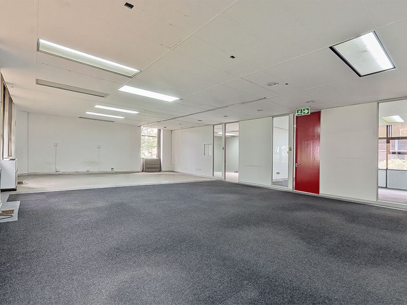 An open-plan commercial office space featuring carpeted flooring, suspended ceilings with recessed lighting, and glass partition walls.