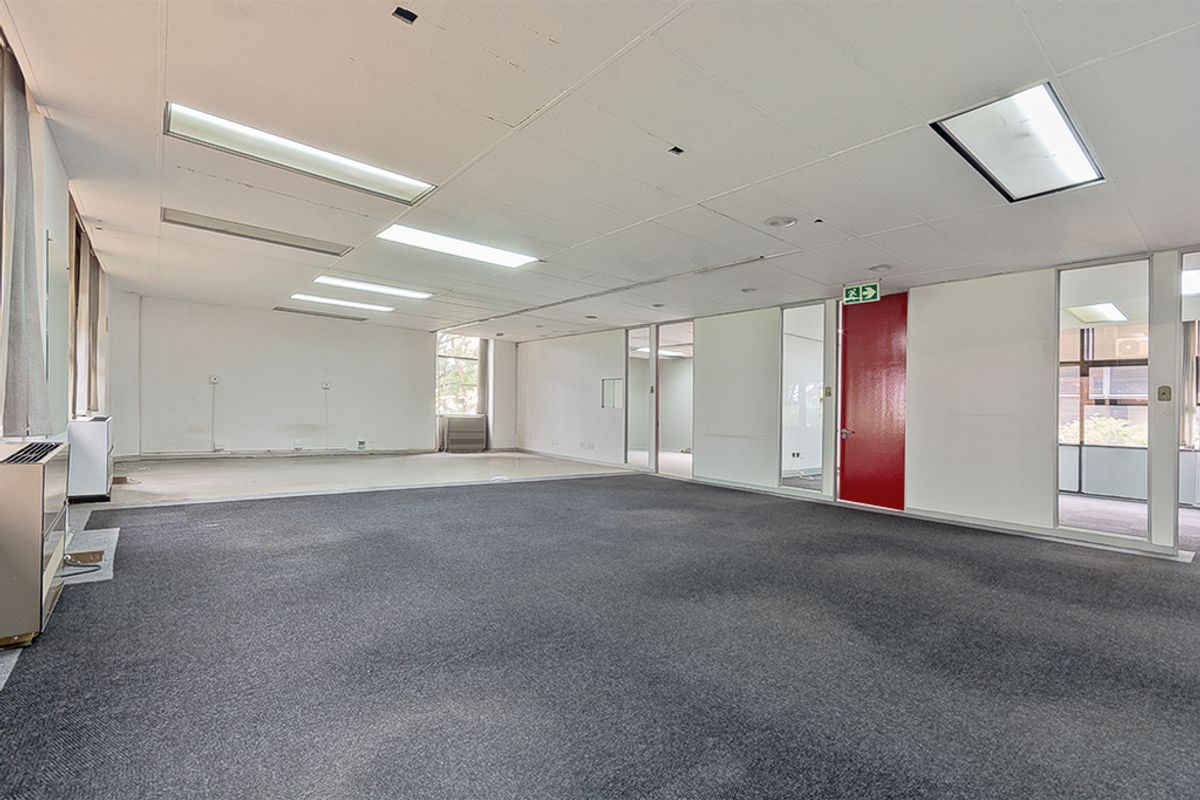 An open-plan commercial office space featuring carpeted flooring, suspended ceilings with recessed lighting, and glass partition walls.