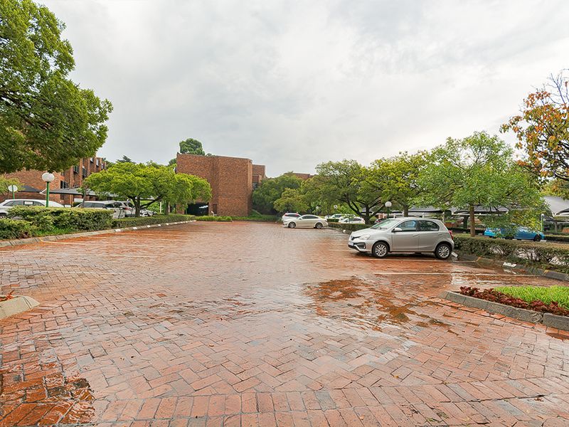 An outdoor commercial parking area featuring brick paving, mature trees, and established landscaping.