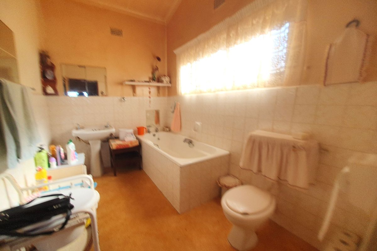 A dated bathroom featuring a pedestal basin, built-in bathtub, and toilet with tiled wall splashbacks and a vaulted ceiling.