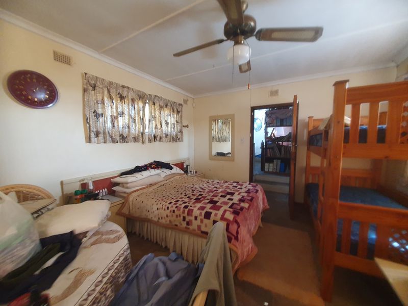 A bedroom featuring a ceiling fan and built-in headboard, providing functional space with access to an adjacent room.