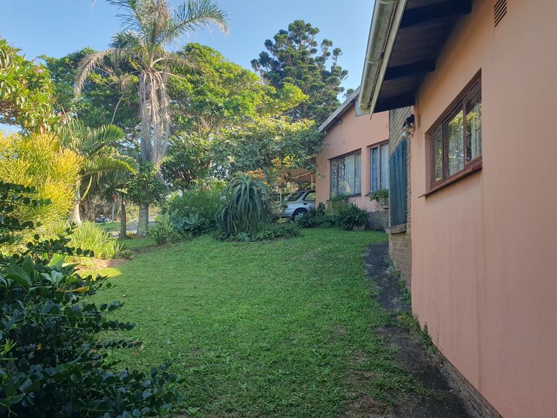 A view of the rear garden featuring a well-established lawn, mature trees, and the side elevation of the house with timber window frames.