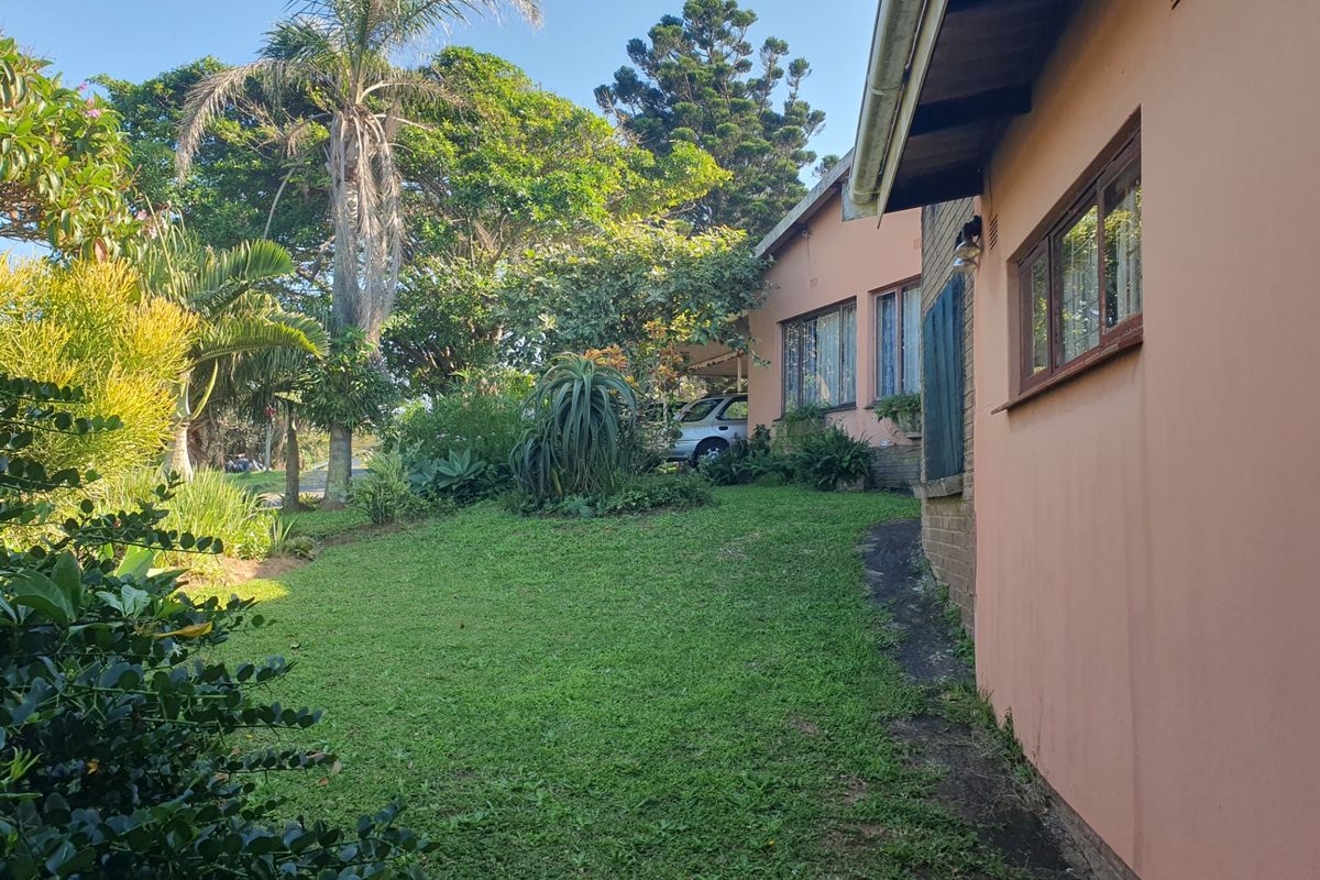 A view of the rear garden featuring a well-established lawn, mature trees, and the side elevation of the house with timber window frames.