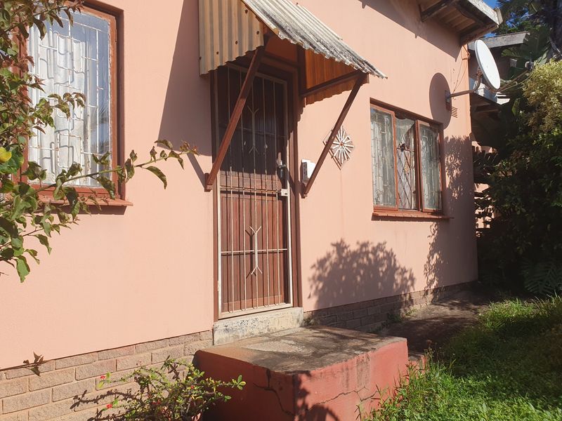 Front entrance of the house featuring a security gate, corrugated metal awning, and brick base foundation.