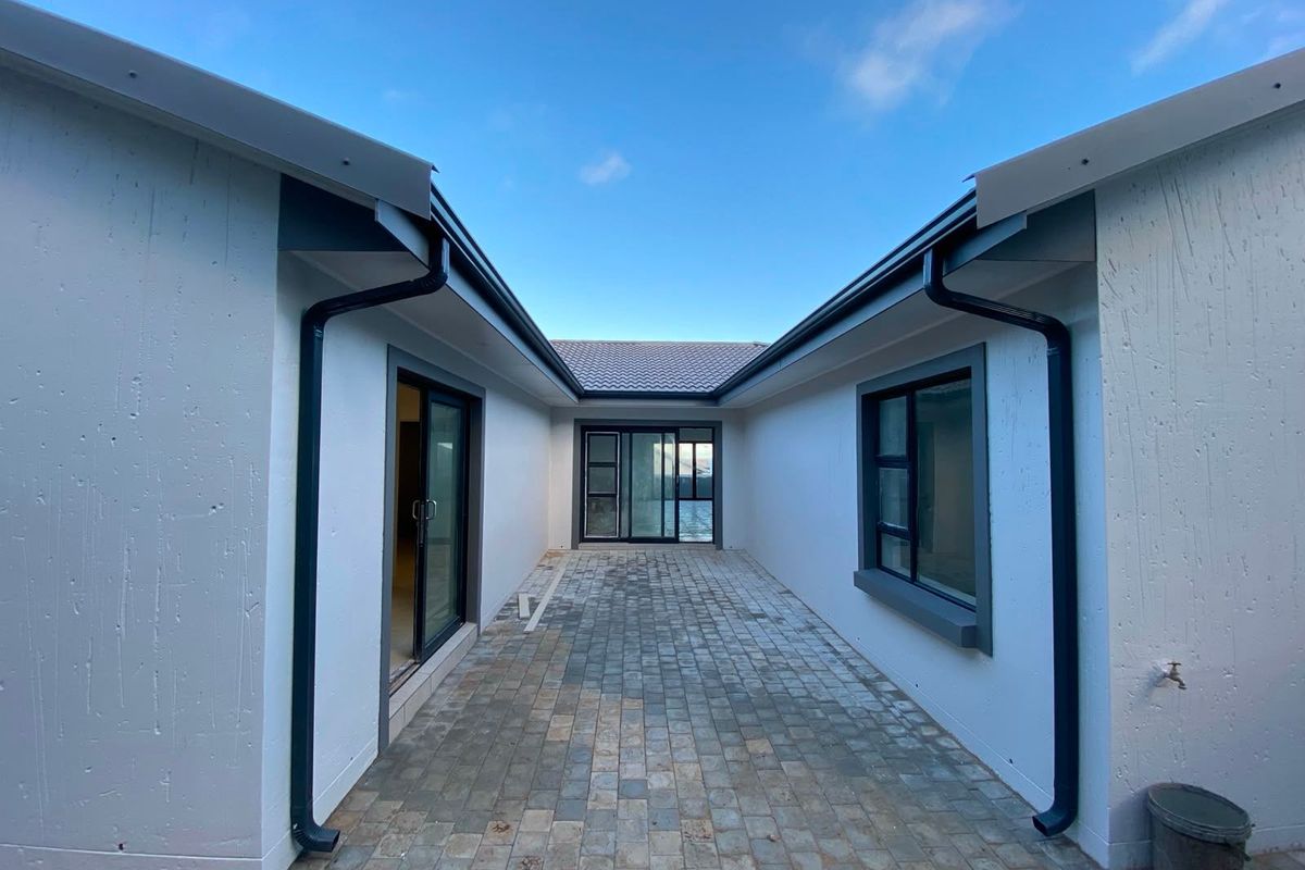 A modern, paved rear courtyard area featuring clean white rendered walls, dark aluminium window frames, and sliding glass door access to the home.