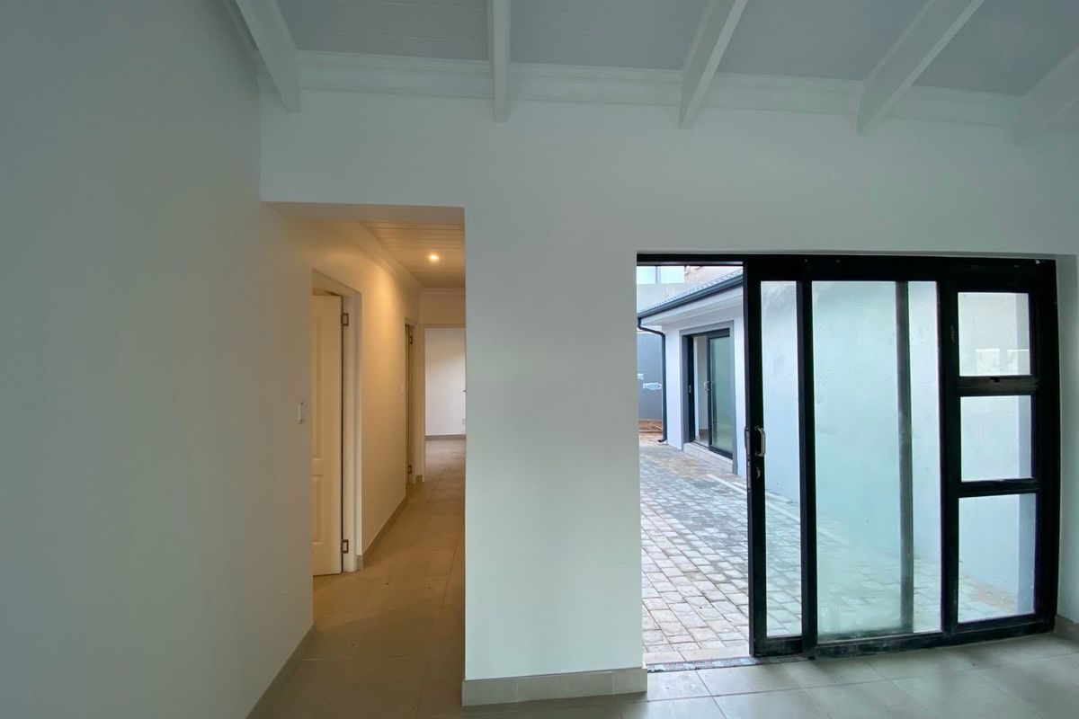 Bright, open-plan living area featuring exposed beam ceilings, tiled flooring, and large sliding glass doors providing direct access to the paved outdoor patio.