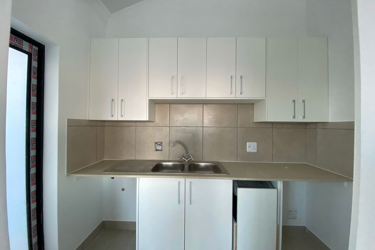 A clean, functional kitchen area featuring white built-in cabinetry, a stainless steel double sink, and neutral tiled backsplash.
