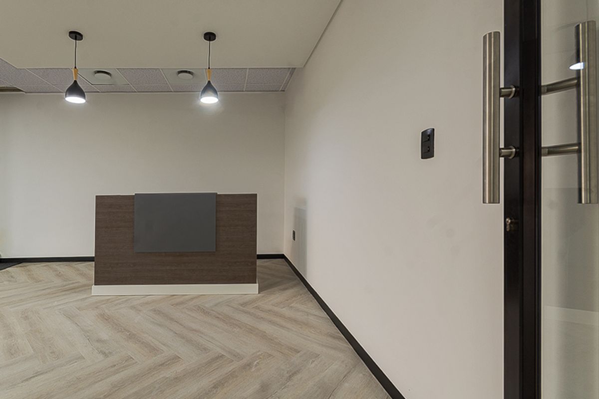 A modern, minimalist office reception area featuring herringbone flooring, a built-in reception desk, and contemporary pendant lighting.