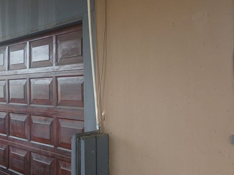Exterior view of a residential garage featuring a wooden sectional door and adjacent wall with visible surface wear.
