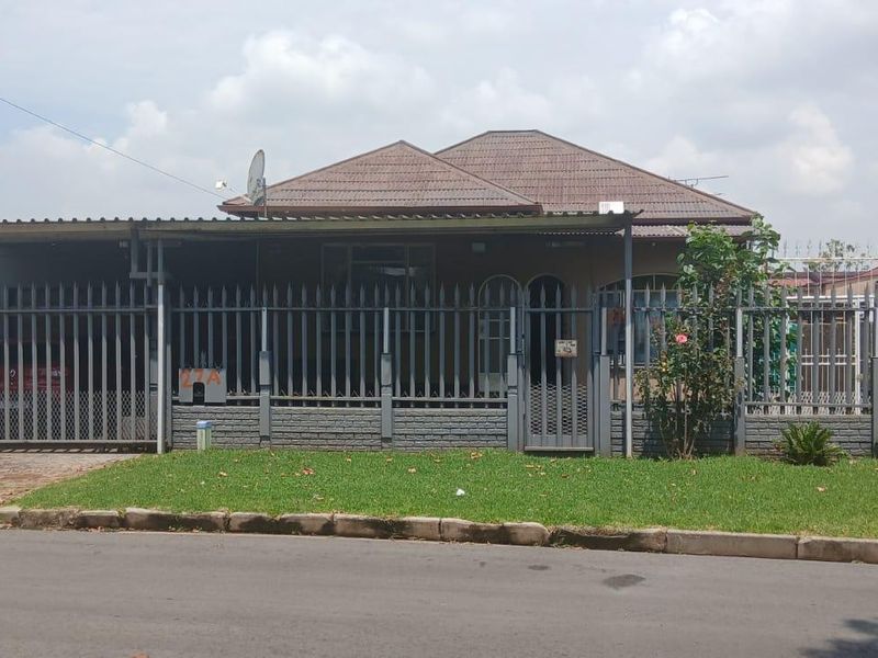 Front elevation of a single-story house featuring a tiled roof, paved driveway, and secure metal perimeter fencing.