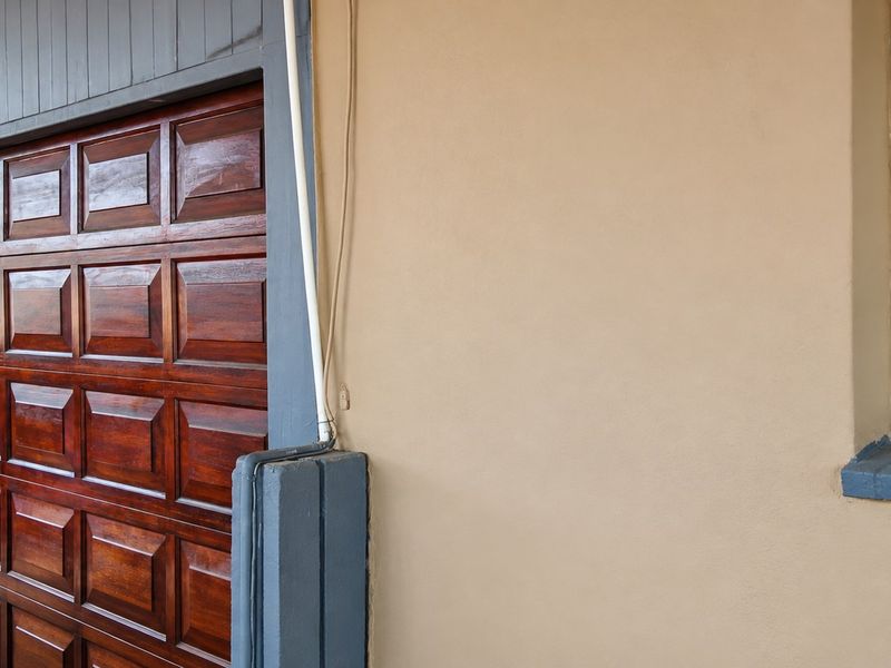 A well-maintained garage exterior featuring a polished wooden sectional door and a window with security bars.