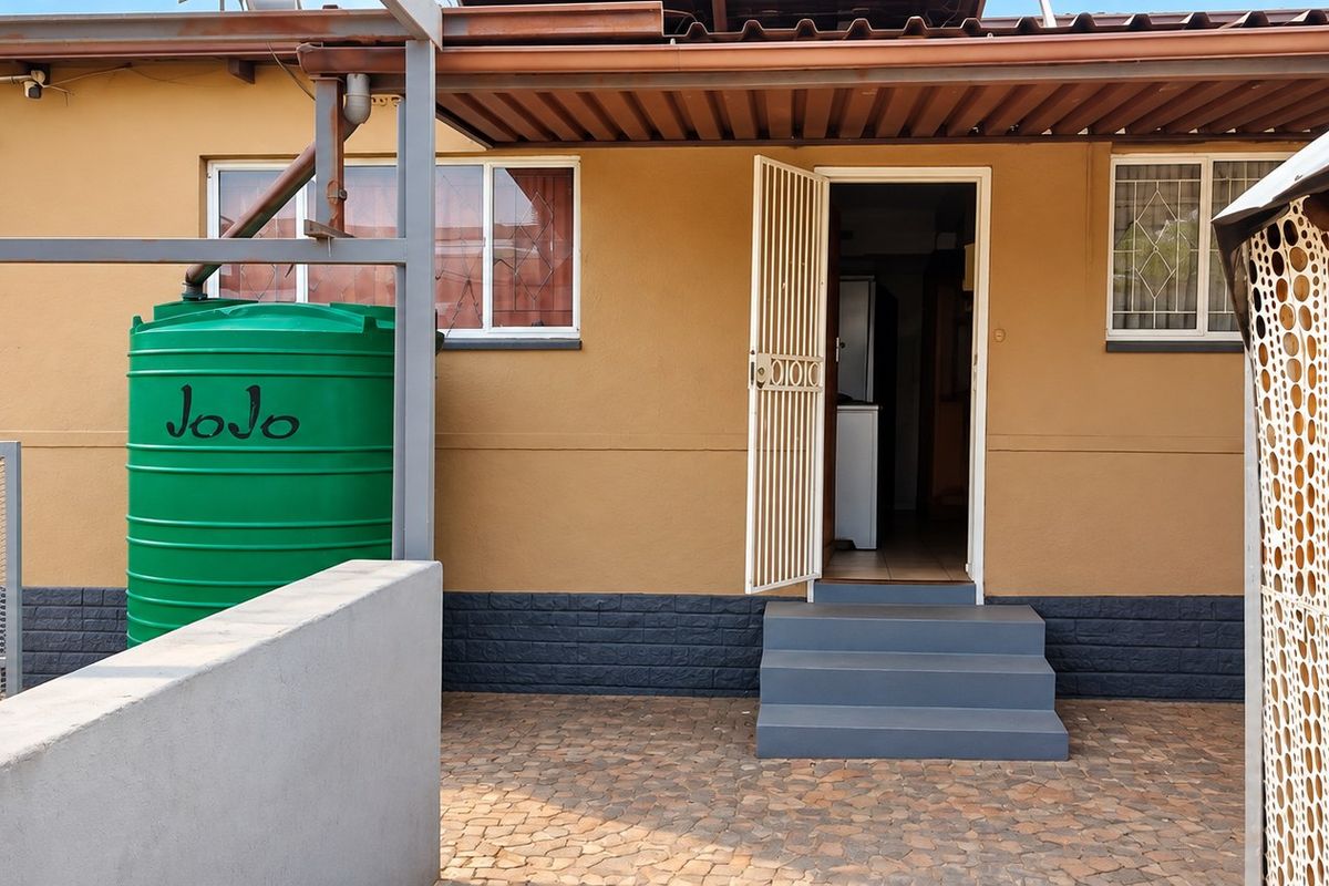 Rear exterior view featuring a paved patio area, security gate, and a water storage tank installed against the building facade.