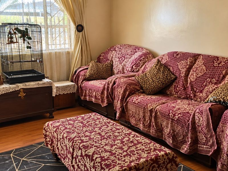 A living room featuring laminate flooring and a window fitted with security bars, providing a functional and lived-in space.