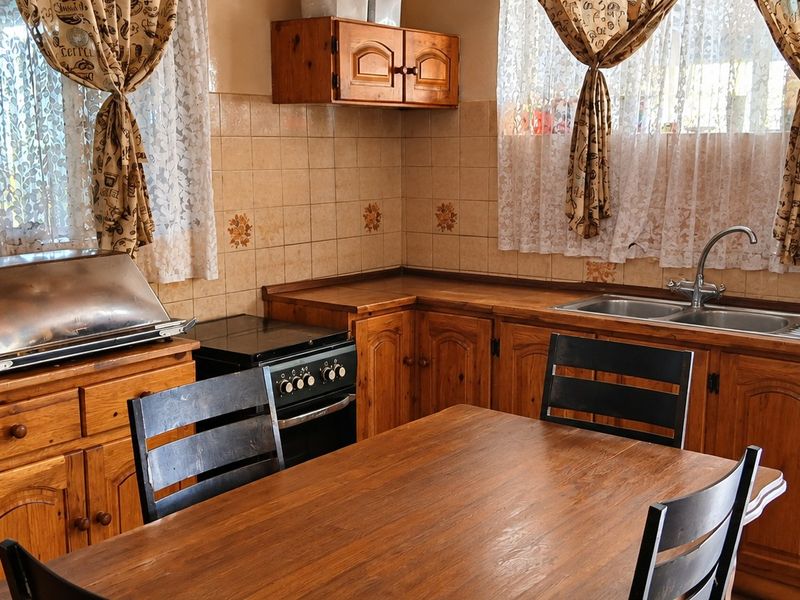 A functional kitchen featuring traditional wooden cabinetry, laminate countertops, a double bowl sink, and a tiled splashback, offering a classic, dated aesthetic.