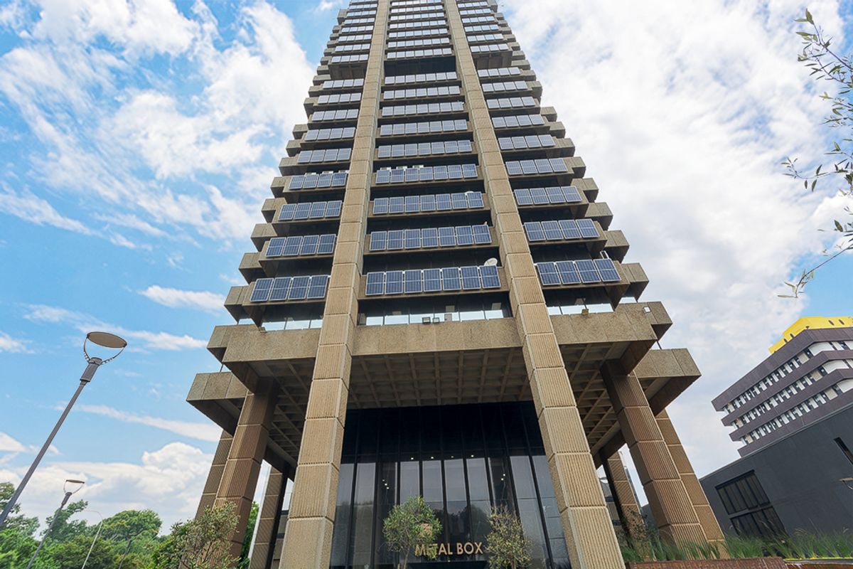 A low-angle view of a high-rise commercial building featuring a concrete structure, glass facade, and integrated solar panels on the exterior.