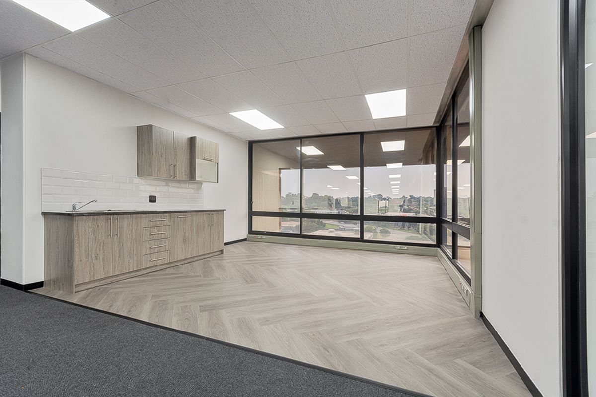 Modern office kitchenette featuring wood-grain cabinetry, subway tile backsplash, herringbone vinyl flooring, and expansive windows providing natural light.