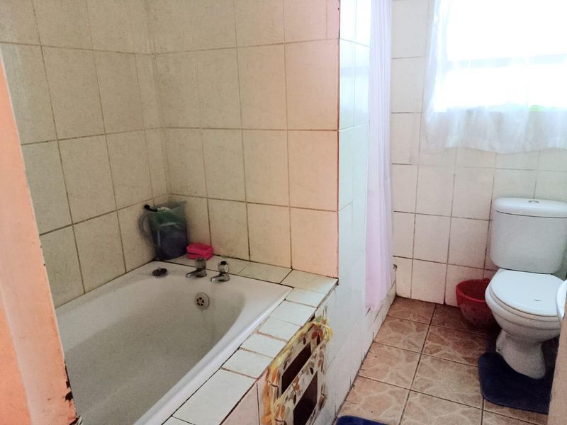 A functional bathroom featuring a built-in bathtub with tiled surround and a standard toilet, requiring cosmetic updates to modernize the space.