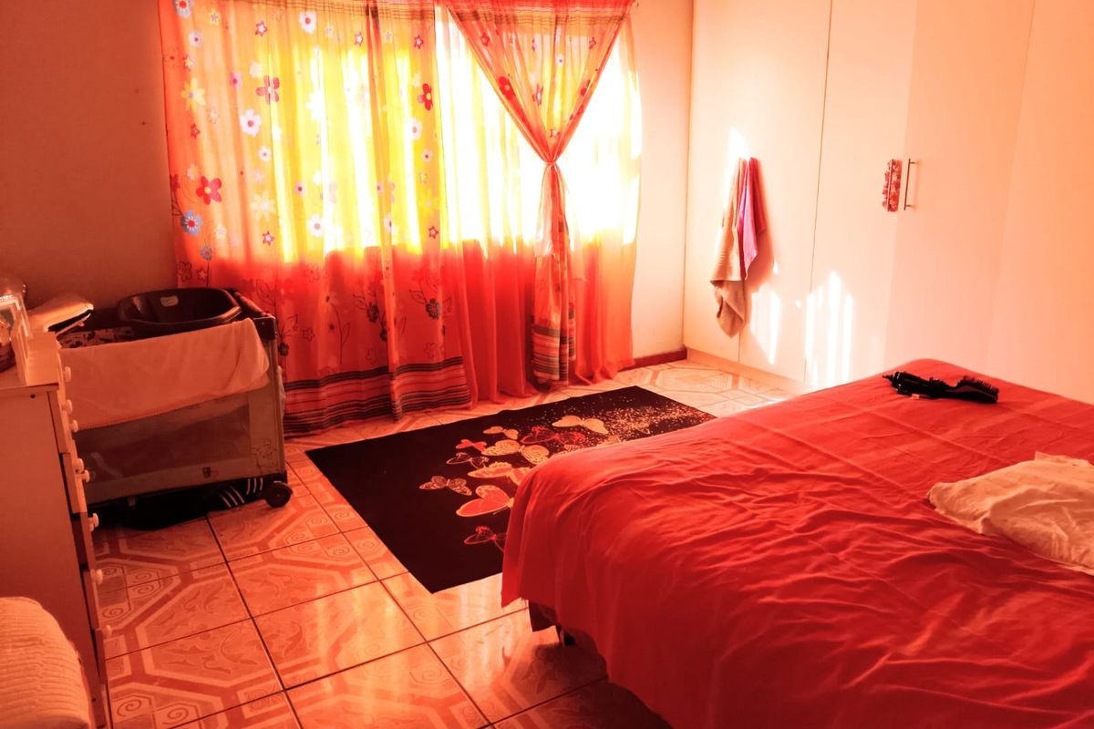 A bedroom featuring tiled flooring and built-in cupboards, illuminated by natural light through the window.