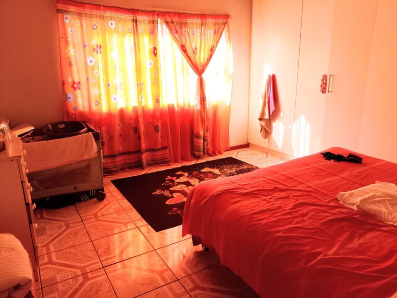 A bedroom featuring tiled flooring and built-in cupboards, illuminated by natural light through the window.