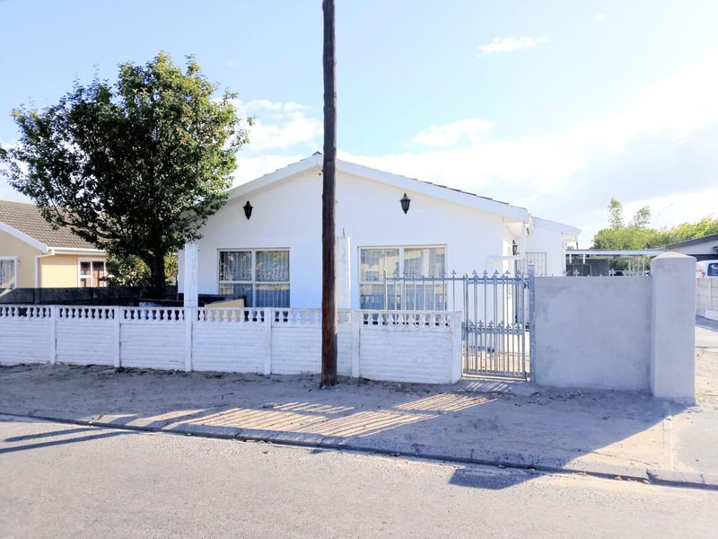 Front view of a single-story residential house featuring a white facade, metal security gate, and a perimeter boundary wall.