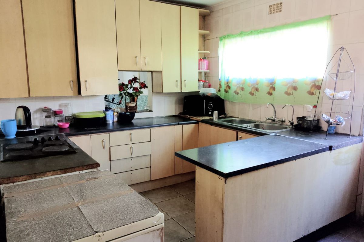 A dated kitchen featuring light-toned cabinetry, laminate countertops, a double sink, and a built-in hob, offering a functional layout with potential for modernization.