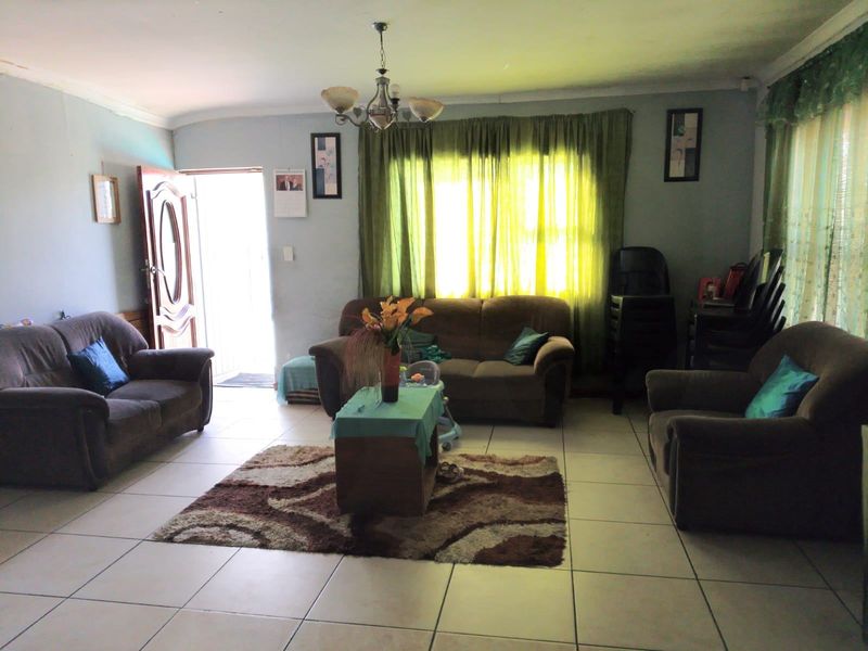 A spacious living room featuring neutral floor tiles, a central chandelier, and natural light entering through the front entrance and window.