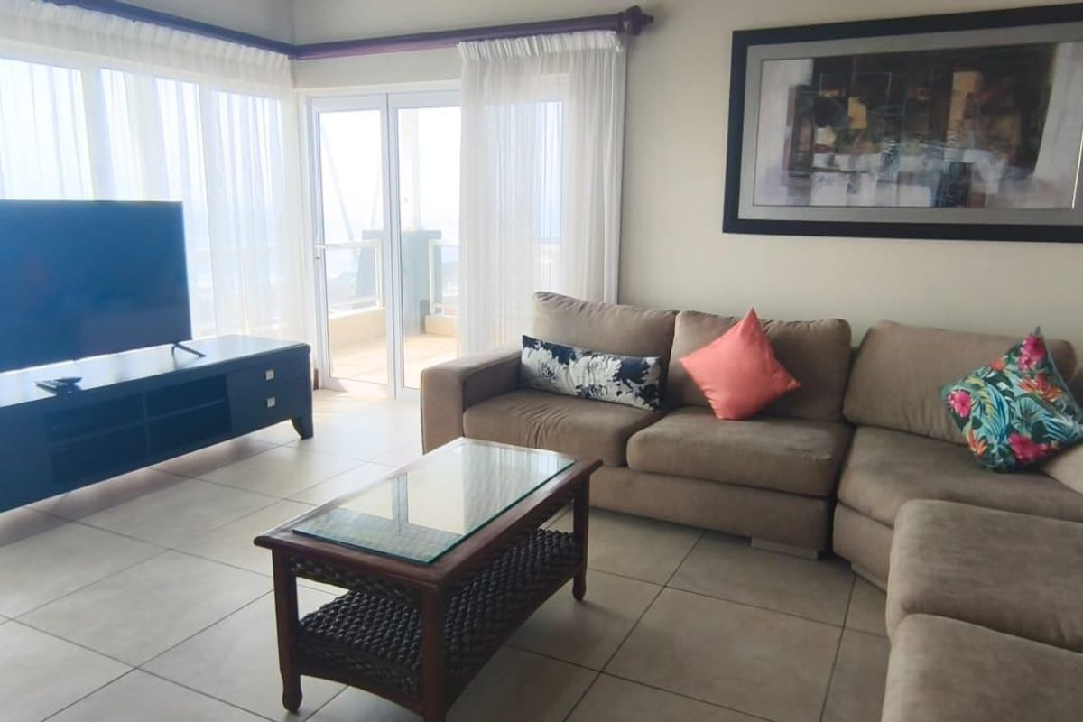 A bright living room featuring large format floor tiles and a sliding glass door providing access to an outdoor balcony area.