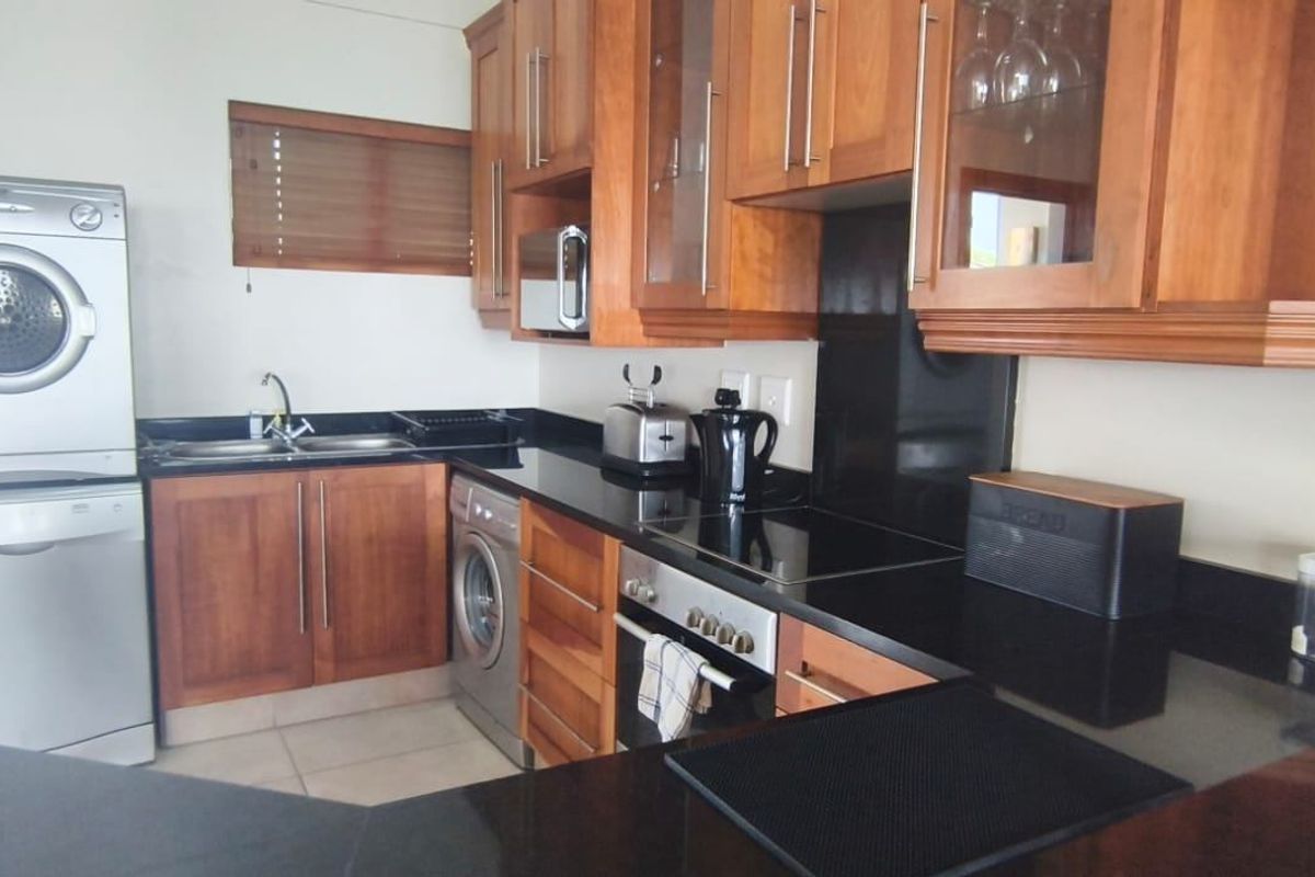 A functional kitchen featuring warm wooden cabinetry, sleek black granite countertops, integrated appliances, and a built-in oven with an electric hob.