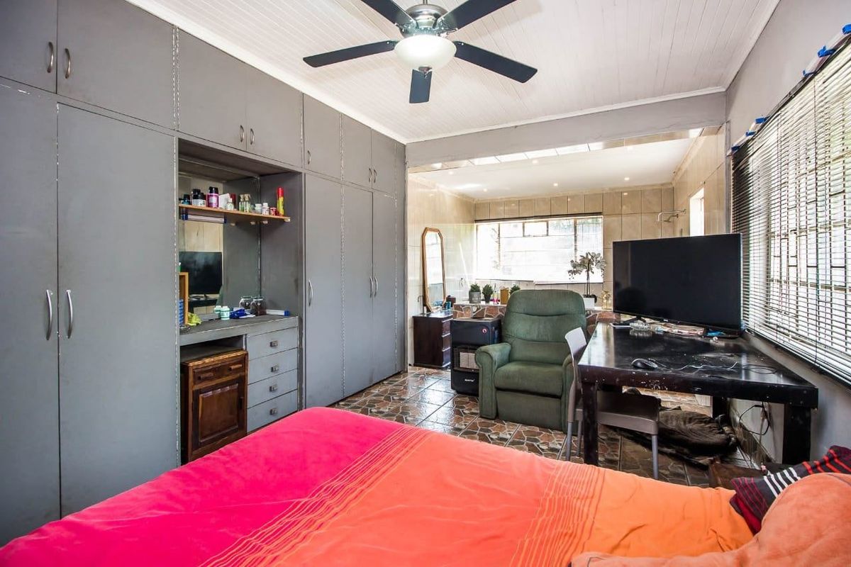 Spacious bedroom featuring extensive built-in cabinetry, a ceiling fan, and tiled flooring, offering a functional layout with potential for modern updates.