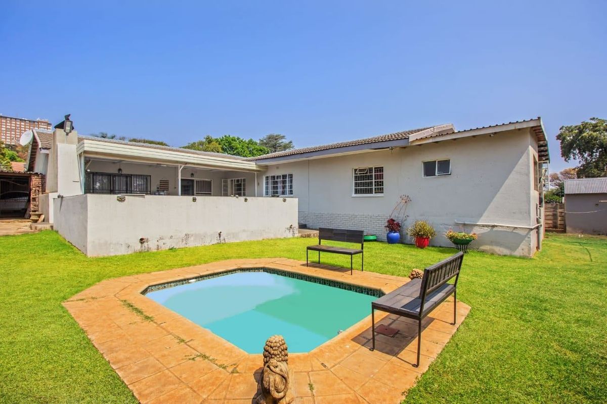 Rear view of the property featuring a swimming pool with tiled surround, a covered patio area, and a spacious lawn.