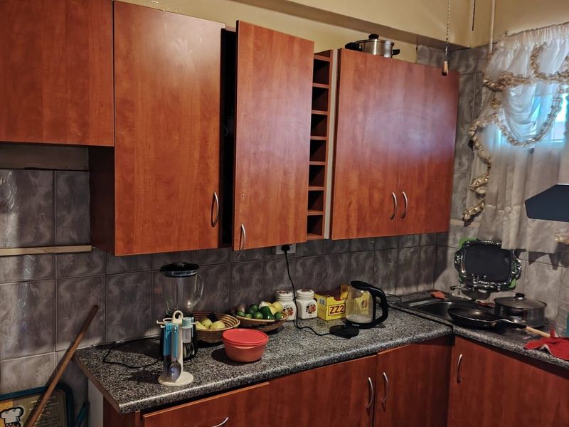 A functional kitchen featuring wood-tone laminate cabinetry, granite countertops, and tiled backsplash, currently showing signs of wear and dated finishes.