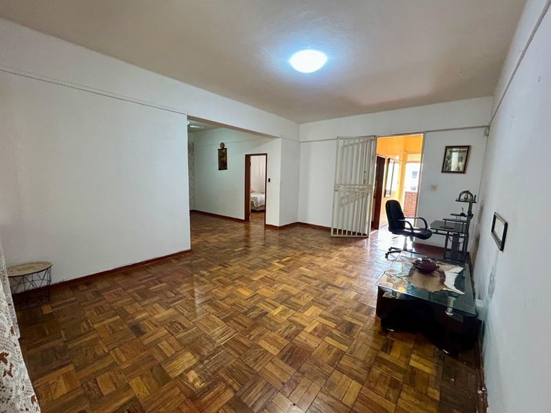 Spacious living area featuring traditional parquet flooring and a security gate leading to an adjacent space.