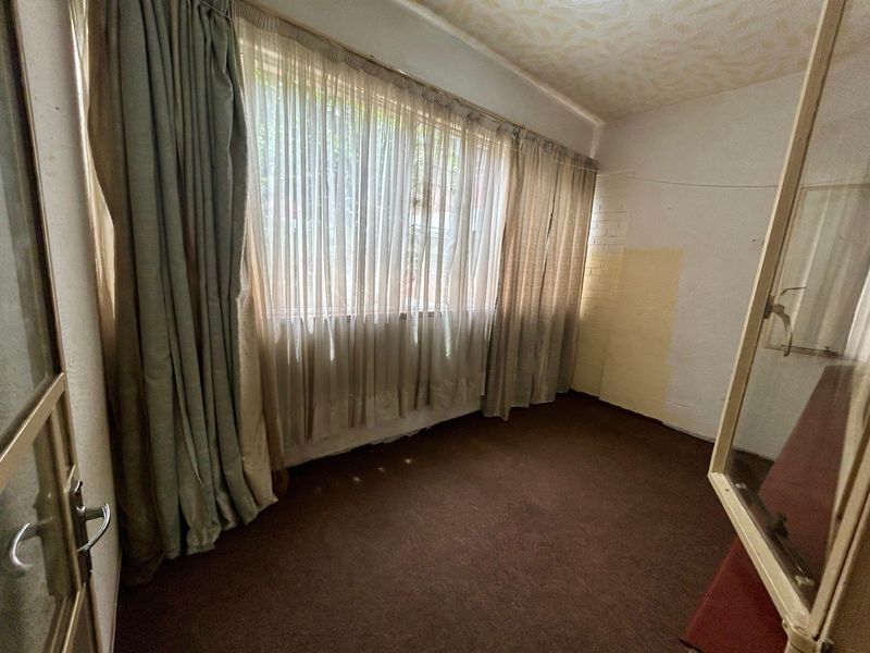 An empty bedroom featuring a large window and textured ceiling, requiring cosmetic updates to the walls and flooring to improve its overall condition.