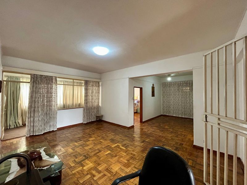Spacious open-plan living area featuring traditional parquet flooring and a secure entrance gate, offering a versatile layout for dining and lounge arrangements.