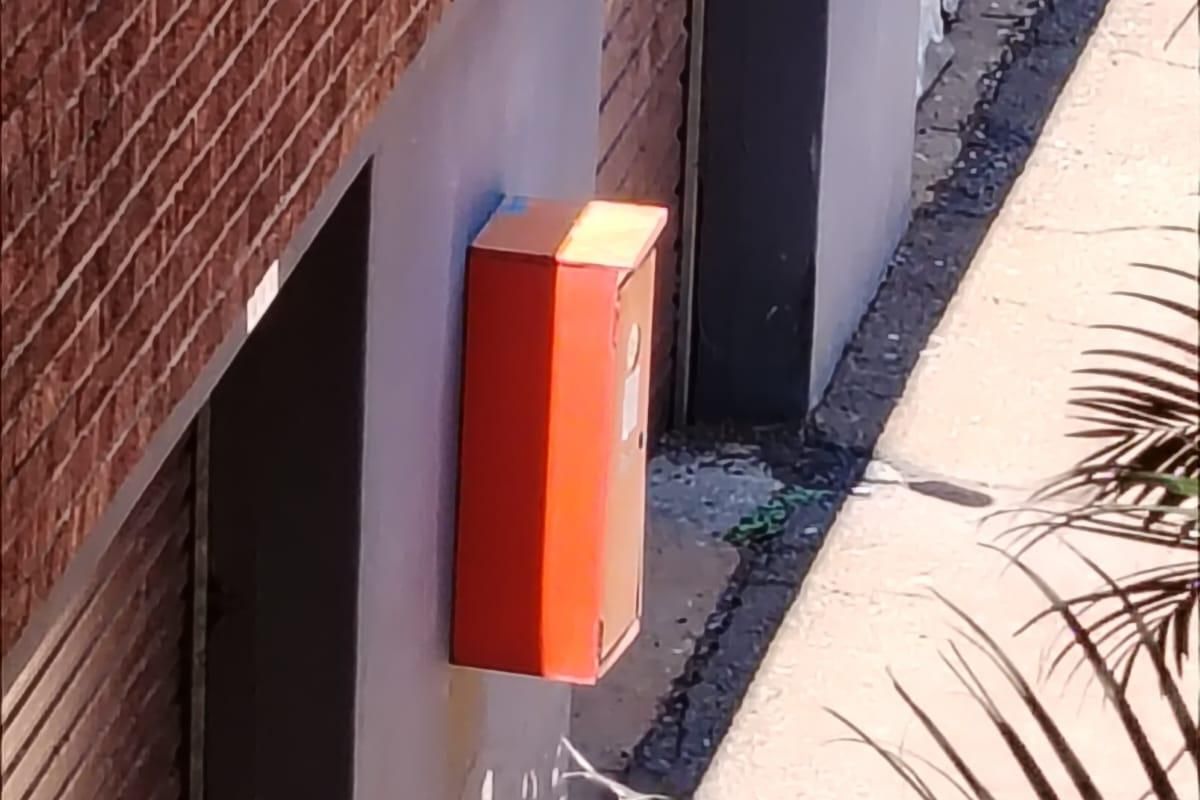 An exterior view of a brick apartment building facade featuring a wall-mounted fire hose reel and visible signs of exterior wall wear.