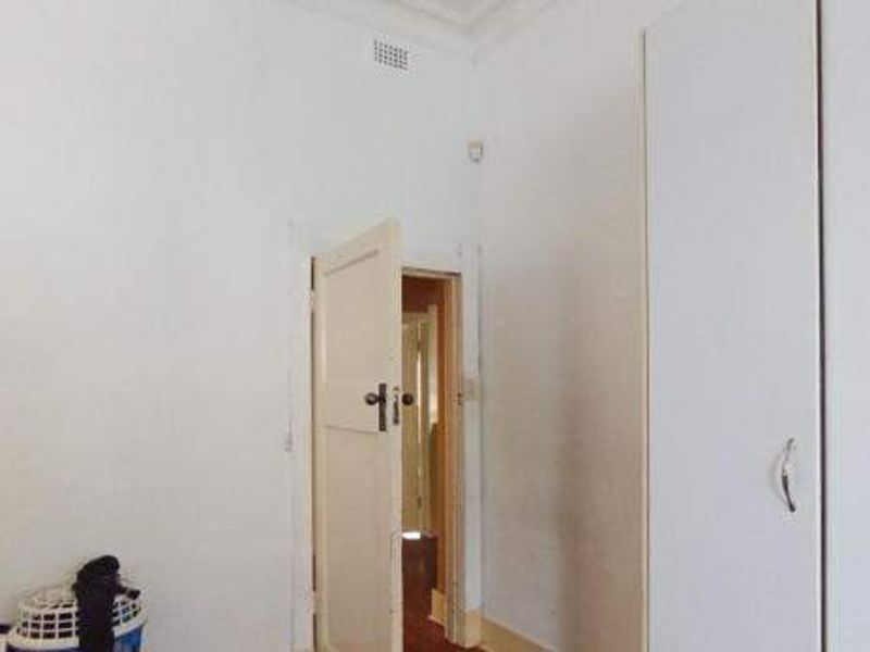 A vacant bedroom featuring built-in wardrobes, decorative cornicing, and original timber door frames, requiring cosmetic updates to improve its overall presentation.