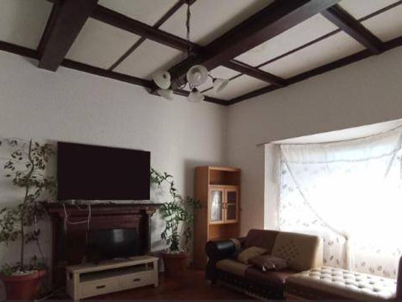 Living room featuring exposed timber ceiling beams, a traditional fireplace mantel, and a large bay window providing natural light.
