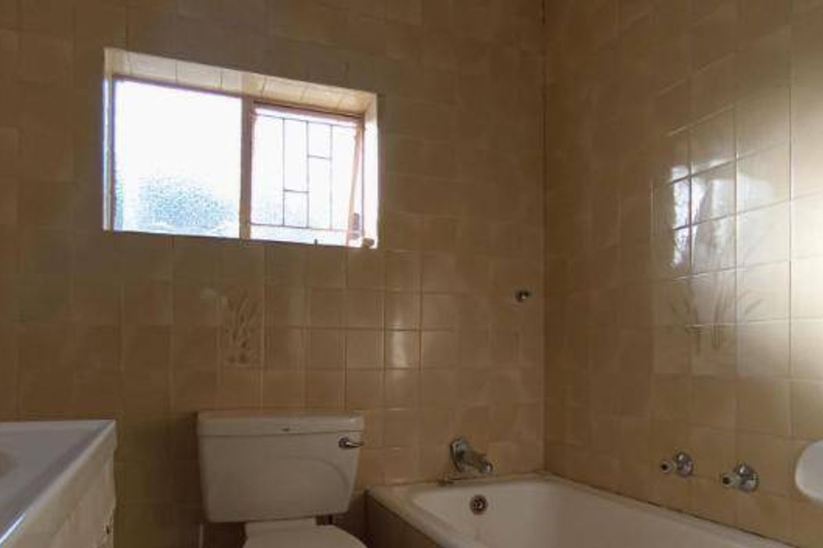 A dated bathroom featuring original ceramic wall tiles, a standard bathtub, pedestal basin, and toilet, awaiting modernization.