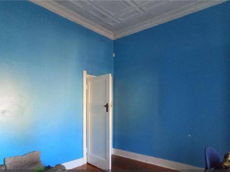A spacious bedroom featuring high ceilings with ornate detailing and original timber flooring, offering a blank canvas for renovation.