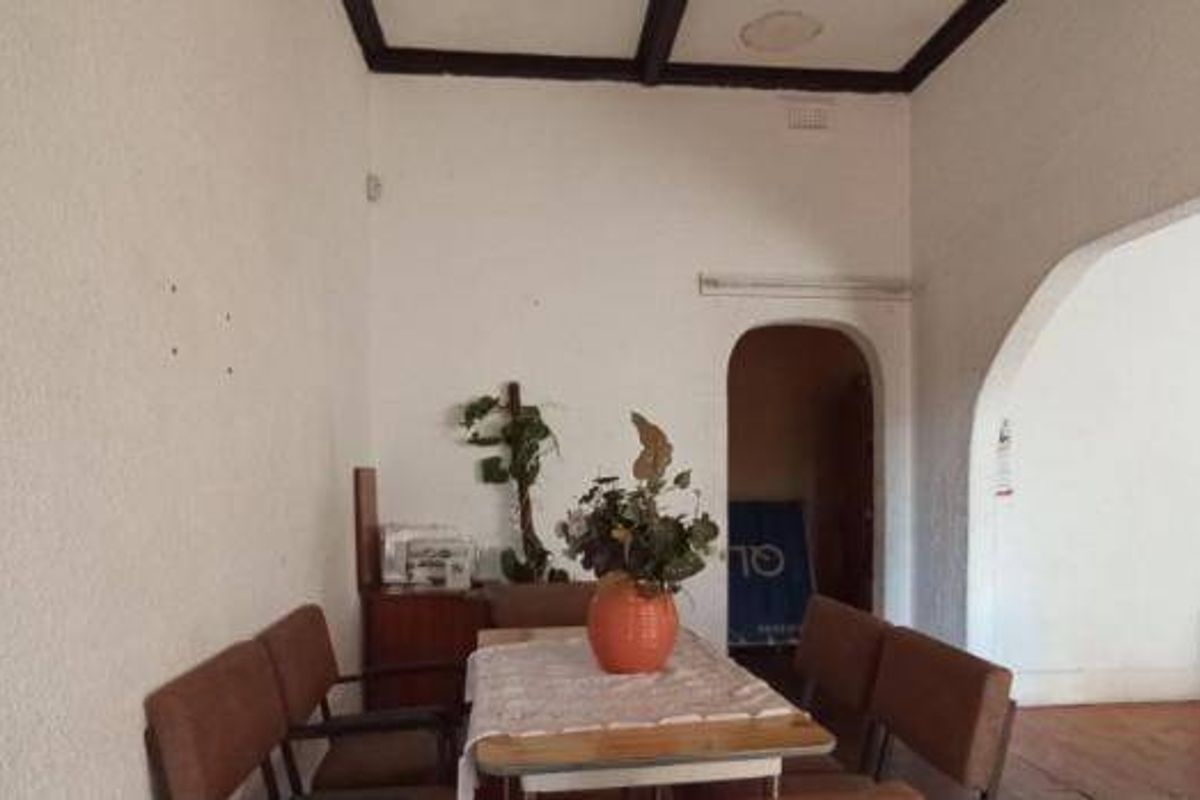 A living area featuring exposed ceiling beams, timber flooring, and an arched doorway leading to an adjacent space.