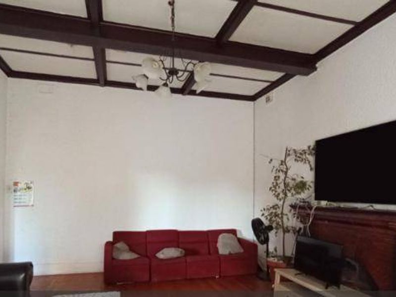 Spacious living room featuring classic exposed timber ceiling beams, hardwood flooring, and a traditional timber fireplace mantel.